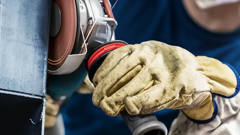 Oseba, ki nosi varnostno opremo, polira kovino z vrtljivim kotnim brusilnikom.